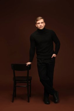 Moda modeli. Koyu kahverengi arka planda sandalyeli yakışıklı bir adam.