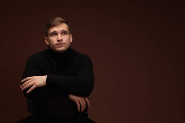 Moda modeli. Koyu kahverengi arkaplana karşı poz veren yakışıklı adam, metin için boşluk