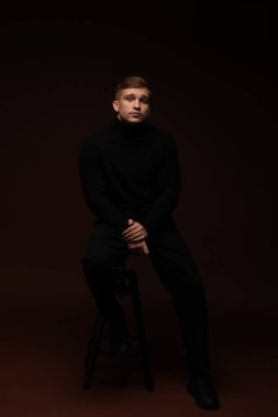 Moda modeli. Koyu kahverengi arka planda poz veren yakışıklı bir adam.