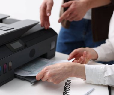 Ofis çalışanları içerideki beyaz masada yazıcı kullanıyor, yakın plan.