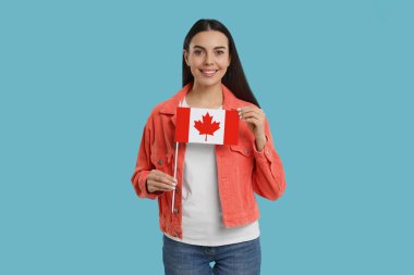 Açık mavi arka planda Kanada bayrağı taşıyan mutlu kadın