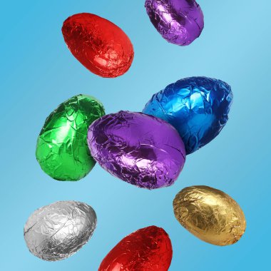 Parlak folyoyla çikolatalı yumurtalar pastel mavi arka plana düşüyor.