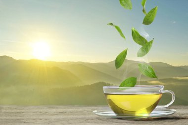 Dağlardaki masada taze demlenmiş çay. Yeşil yapraklar fincanın üzerinde uçuyor