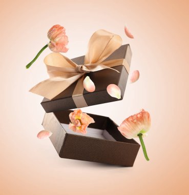 Hediye kutusu ve çiçekler bej renkli arka planda havada uçuşuyor.