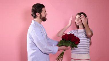 Romantik bir randevu. Adam pembe arka planda bir buket kırmızı gülle sevgilisine sürpriz yapıyor.