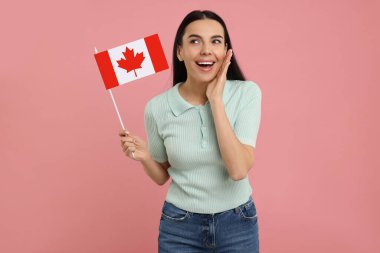 Pembe arka planda Kanada bayrağı taşıyan mutlu kadın.