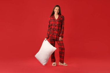 Kırmızı arka planda yastıklı şık pijamalı mutlu kadın.