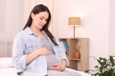 Hamile kadın evde yatakta oturuyor.