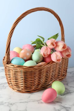 Boyanmış Paskalya yumurtaları ve hasır sepetteki güzel laleler beyaz mermer masada, yakın plan.