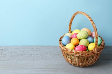 Hasır sepetin içine boyanmış Paskalya yumurtaları açık mavi arka planda gri ahşap masa üzerinde. Metin için boşluk