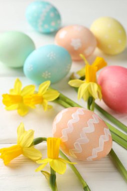 Boyalı Paskalya yumurtaları ve beyaz ahşap masaya güzel nergisler, yakın plan.