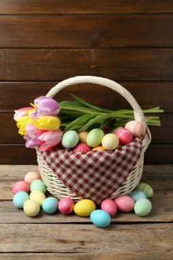 Hasır sepete boyanmış Paskalya yumurtaları ve ahşap masada güzel laleler.