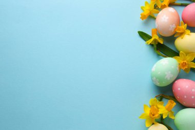 Boyanmış Paskalya yumurtaları ve açık mavi arka planda güzel nergisler. Metin için boşluk