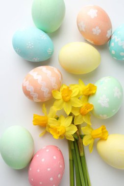 Beyaz arka planda boyanmış Paskalya yumurtaları ve güzel nergisler.