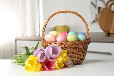 Beyaz masa üzerinde boyanmış yumurta ve lalelerle dolu Paskalya sepeti.