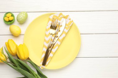 Paskalya kutlaması. Çatal bıçak takımı, çiçekler ve beyaz ahşap masaya boyanmış yumurtalar, düz yatak. Metin için boşluk
