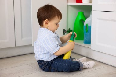 Evde çocuk güvenliği. Küçük çocuk mutfakta temizlik ürünleriyle dolap açıyor.