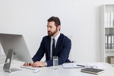 Beyaz duvarın yanındaki masada bilgisayarla çalışan bir işadamı.