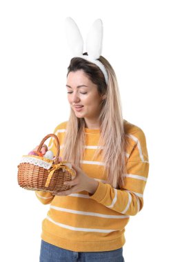 Paskalya kutlaması. Saç bandı takmış, tavşan kulaklı, hasırdan sepet dolusu beyaz arka planda boyalı yumurtaları olan gülümseyen bir kadın.