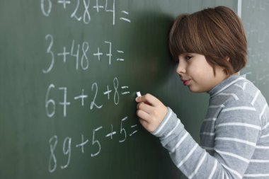 Okullu çocuk sınıfta tahtada matematik yapıyor.