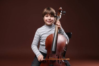 Kahverengi arka planda keman çalan sevimli küçük çocuk.