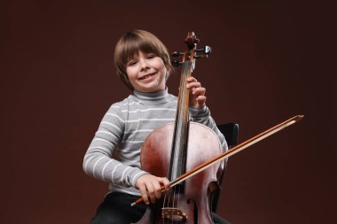 Kahverengi arka planda keman çalan sevimli küçük çocuk.