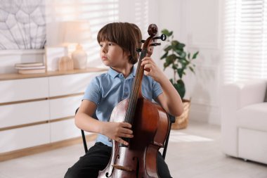 Evdeki sandalyede keman çalan küçük çocuk.