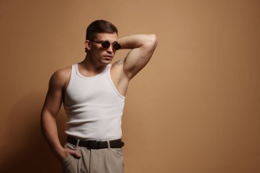 Moda modeli. Bej arkaplanda poz veren güneş gözlüklü yakışıklı adam, metin için boşluk