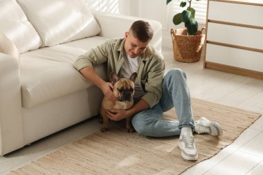 Evdeki kanepenin yanında tatlı köpeğiyle rahatlayan genç bir adam.