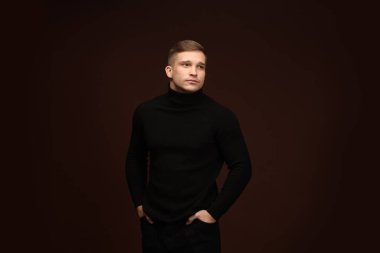 Moda modeli. Koyu kahverengi arka planda poz veren yakışıklı bir adam.