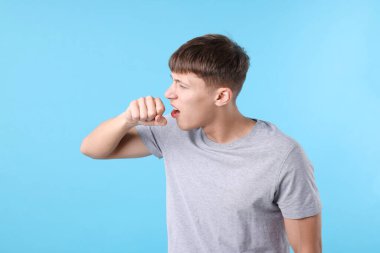 Açık mavi arka planda öksüren hasta genç adam, mesaj için yer var. Soğuk Semptom