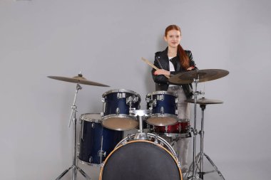 Açık gri arka planda bagetleri ve davulları olan genç bir kız.