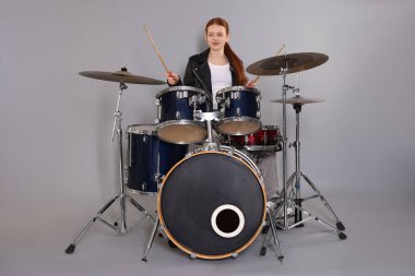 Açık gri arka planda bagetleri ve davulları olan genç bir kız.