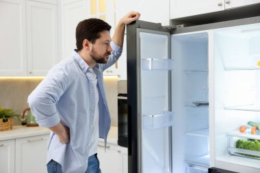 Mutfaktaki boş açık buzdolabının yanındaki adam.
