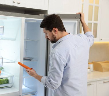 Havuçlu adam mutfakta buzdolabı açık.