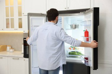 Adam mutfaktaki açık buzdolabına bakıyor.