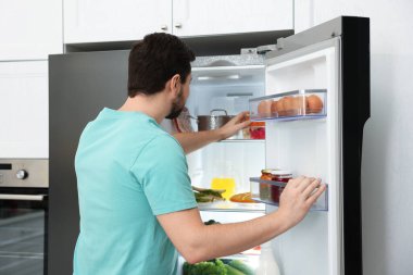 Adam mutfaktaki buzdolabından yiyecek alıyor.
