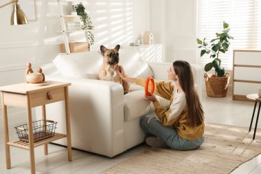 Şirin köpeği ve oyuncağıyla evdeki kanepenin yanında dinlenen bir kadın.