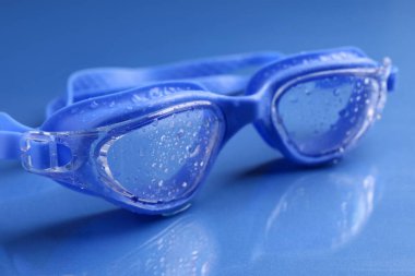 Mavi yüzeyde su damlaları olan yüzme gözlükleri, yakın plan.