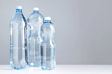 Beyaz masada gri arkaplan ile farklı boyutlarda su şişeleri, metin için boşluk