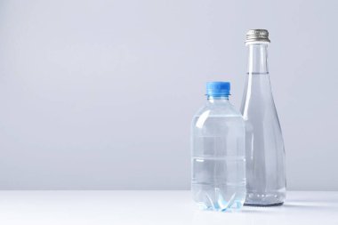 Beyaz masada gri arkaplan ile farklı boyutlarda su şişeleri, metin için boşluk