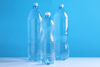 Açık mavi arka planda beyaz masada bir şişe taze su