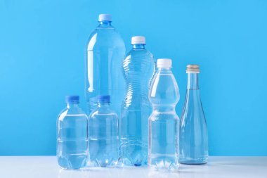 Açık mavi arka planda beyaz masada farklı boyutlarda su şişeleri