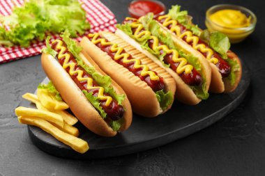 Lezzetli sosisli, ketçap, hardal, marul ve patates kızartması siyah masada, yakın plan.