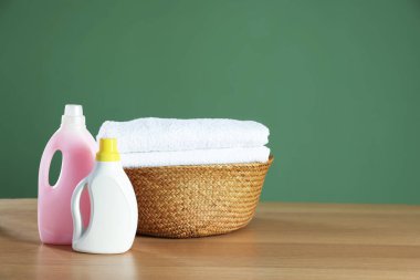 Ahşap masanın üzerinde havlular ve deterjanlar olan çamaşır sepeti koyu yeşil arka planda, metin için boşluk
