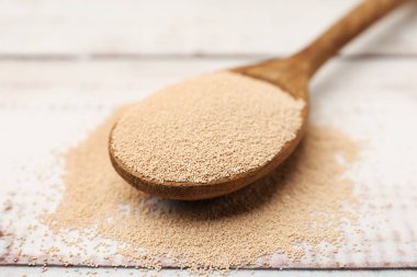 Beyaz ahşap masada kaşıkla kuru maya, yakın çekim.