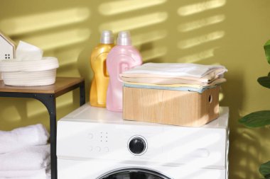 Çamaşır sepetinin içinde çamaşır makinesinin üzerinde katlanmış temiz kıyafetler var.