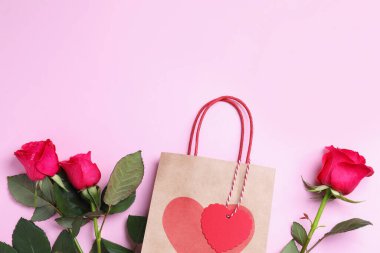 Kağıt torba ve pembe arka planda güller, düz yatış. Metin için boşluk