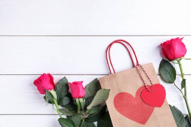 Beyaz ahşap arka planda güller olan hediye çantası, düz yatak ve metin için yer. Sevgililer Günü
