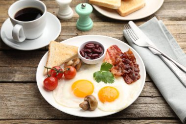 Geleneksel İngiliz kahvaltısı. Lezzetli, güneşli tarafı domuz pastırmalı, kırmızı fasulyeli, domatesli, mantarlı ve ahşap masada servis edilen kızarmış ekmekli yumurtalar.
